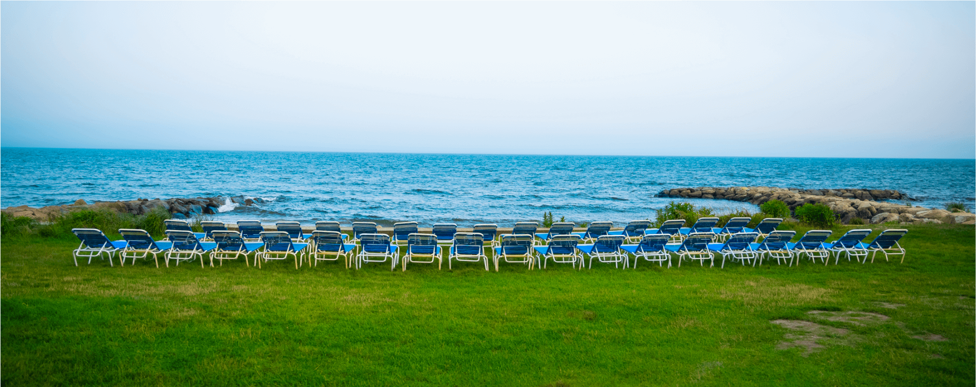 A row of blue and white beach chairs on a grassy lawn overlooking the ocean.