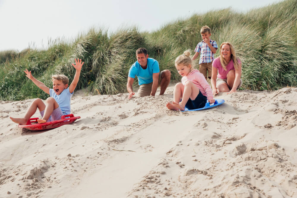 A family sliding down sand dunes, one of the unique things to do in the summer on Cape Cod.
